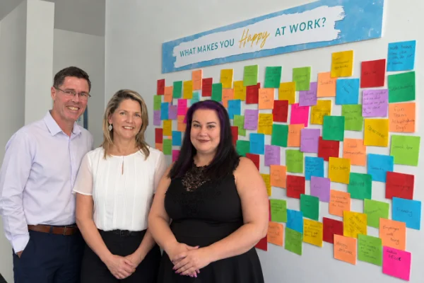 Wardle partners employees in front of what makes us happy board